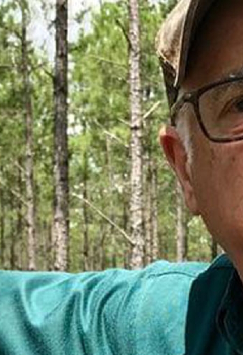 Salem Saloom leans against a longleaf pine tree.