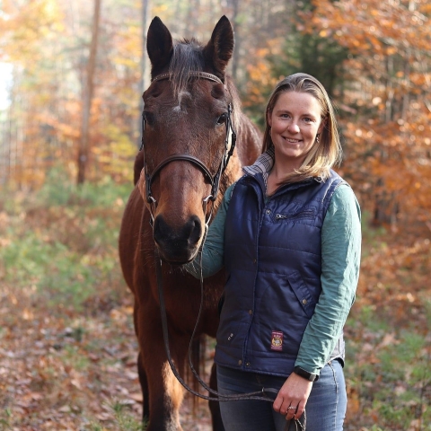 Bri Benvenuti, refuge biological technician at Rachel Carson National Wildlife Refuge, poses with her horse Marshall in fall with colorful leaves framing the two.