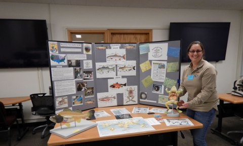 Photo of Lacey Hopper holding dissecting frog demo at Bozeman Fish Health Center outreach table