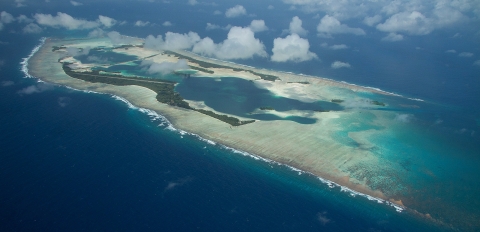 Aerial view of an island atoll surrounded by sandy reef in the deep blue ocean
