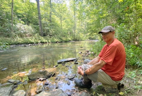 A man sitting alongside a creek.