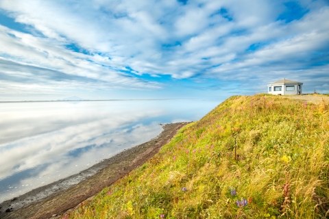 a white gazebo on a bluff looks over calm water reflecting clouds