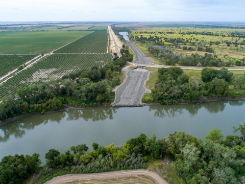 Aerial image of a river surrounded by trees, with crop land and wilderness divided by a road on one side
