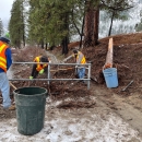 three people in safety vests move small woody debris into into large trash cans at the LNFH ADA fishing platfoorm
