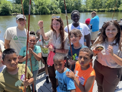 Youth pose with a fish and U.S. Fish and Wildlife Service staff at the 2024 Cops and Bobbers Fishing Program