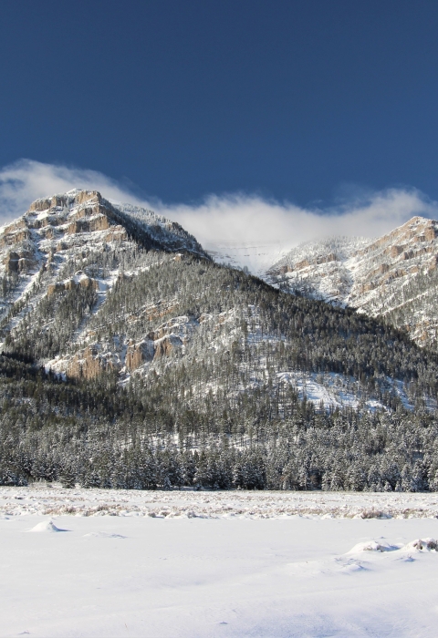 Snow blankets foothills and mountains under blues skies as wispy clouds form atop mountain peaks.