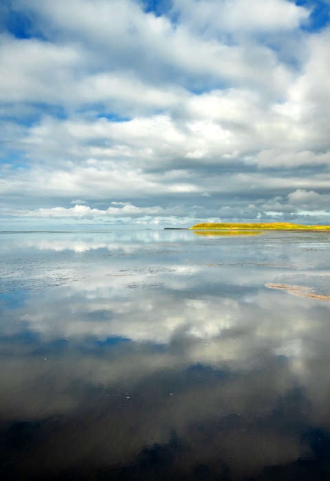 clouds reflect in calm water along coastline