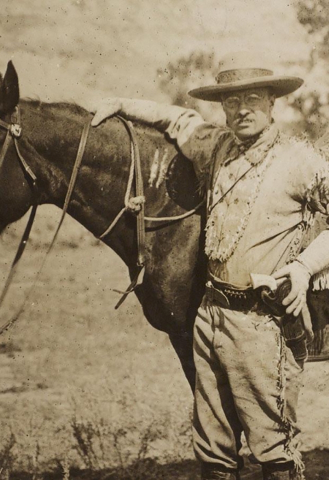 President Theodore Roosevelt poses with his horse on a prairie