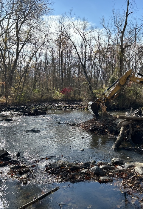 An excavator removing remnants of a dam from a river