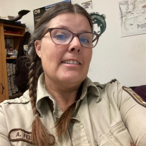 A woman wearing glasses with braided brown hair smiles for the camera.