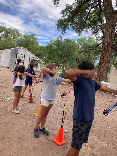 Five Nature Ninos students line up to shoot arrows at archery targets.