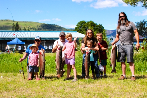 A group of adults with children show off the large trout they have just caught on a sunny June day.