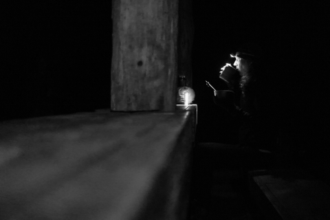 Woman sitting in the darkness, holding a bowl and lifting a mug to her lips