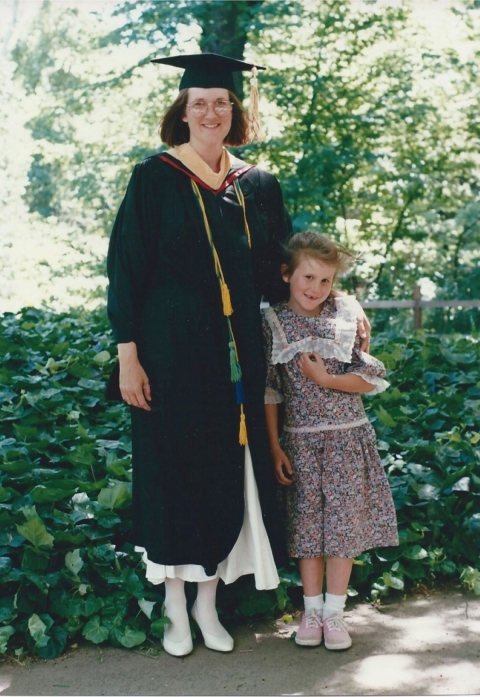 A woman wearing a black cap and gown stands next to a young girl wearing a flowery dress.