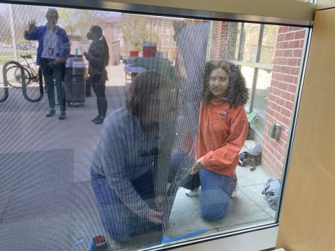 View through a window of two people applying a decal to prevent bird collisions