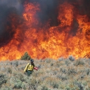 A firefighter walks facing away from a fire burning behind him