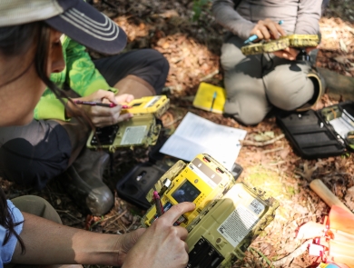 Group of people sitting on a forest floor holding electronic devices