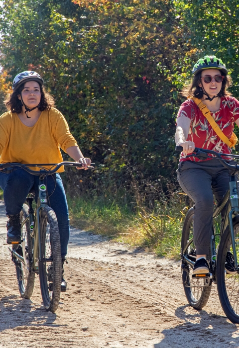 Two woman in bright clothing and helmets riding down a dirt road on electric assisted mountain bikes