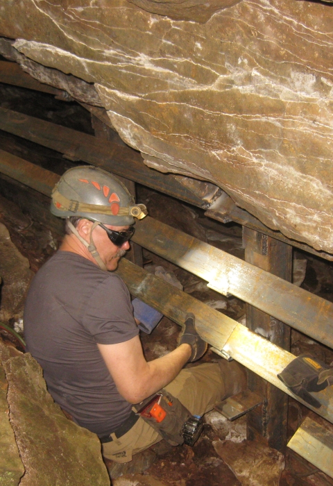 A man in a hard hat builidng a wooden barrier inside a cave.