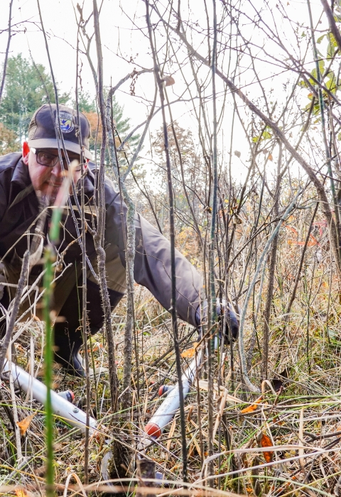 Man kneeling down, using loppers to cut small stems