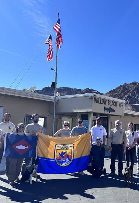 People in front of building holding USFWS flag and fish pennant, US flags fly from building 