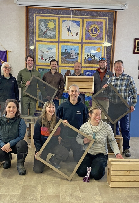 Fourteen people pose for a photo holding wooden boxes and frames with screens.