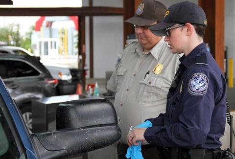 A wildlife inspector and a border protection agent stand next to a car speaking to a driver.