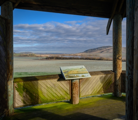 Interpretive sign in the foreground and valley hills on a cloudy day in the background.