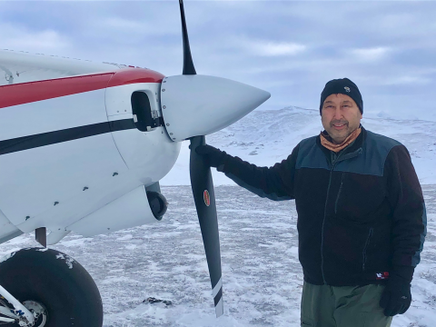 A pilot poses with his single engine plane's propeller in a snow covered treeless landscape