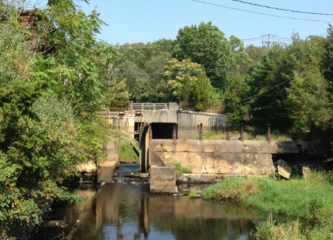 A dilapidated dam on a river in the middle of much vegetation.