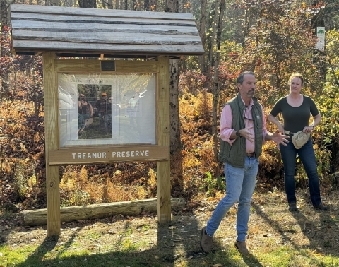 a white man and white woman stand next to a wooden kiosk with a map and the name Treanor Preserve