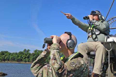 2 men sitting in boat using binoculars, using headphones