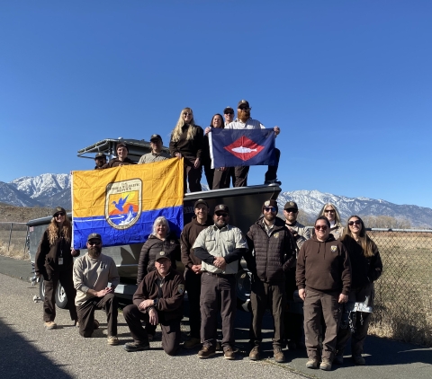 FWS staff on and around boat on trailer on land hold FWS flag, fish pennant 