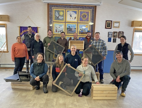 Fourteen people pose for a photo holding wooden boxes and frames with screens.