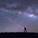 The silhouette of a hiker walking with the night sky illuminating them 