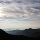 Rolling, forest-covered mountains beneath a partly cloudy sky