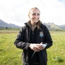 A scientist wearing a U.S. Fish and Wildlife Service jacket holds an Aleutian tern in front of distant mountains.