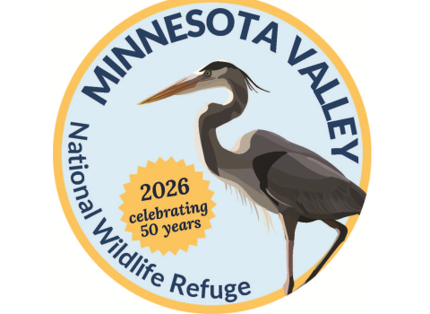 Blue heron stands on one leg in front of light blue background, with Minnesota Valley National Wildlife Refuge 50 Years text around outside of image