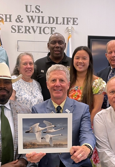 A group of people pose with the winning artwork depicting trumpeter swans.
