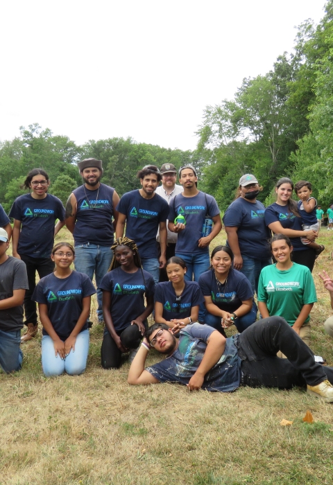 a group of people wearing purple and green shirts standing in a green field of a nature park