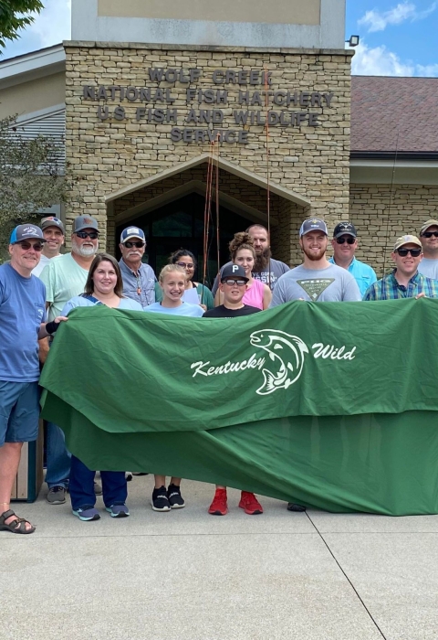 Group photo of people holding a banner in front of facility