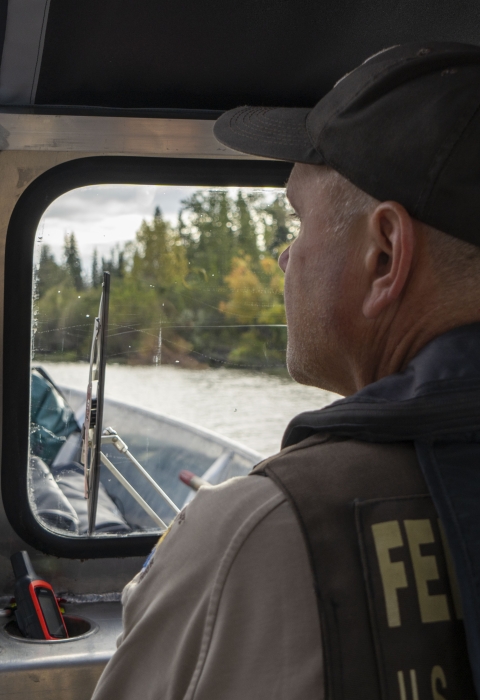 close up of a unformed officer drives a boat with a river in the background
