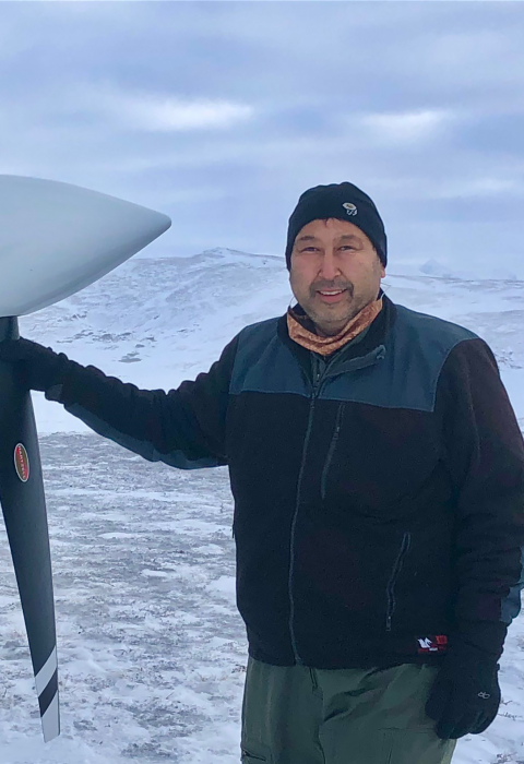 A pilot poses with his single engine plane's propeller in a snow covered treeless landscape