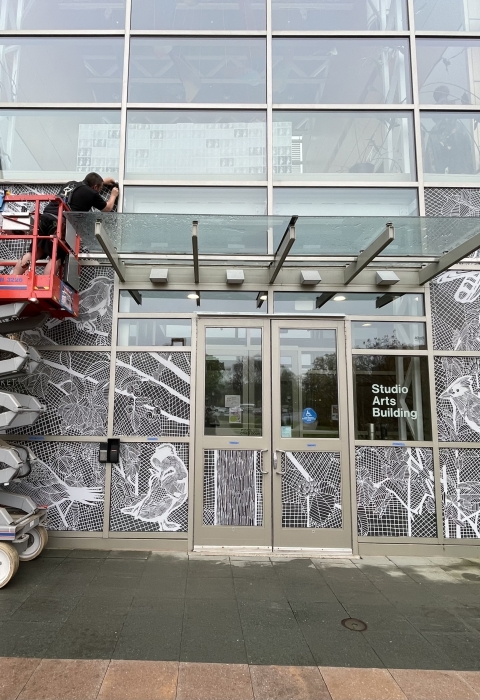 Two people on a construction lift apply decals to the front of a building