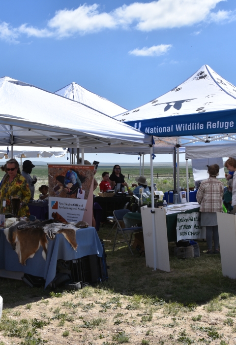 Shade tents with activities set up in a field, staffed by wildlife refuge staff and partners