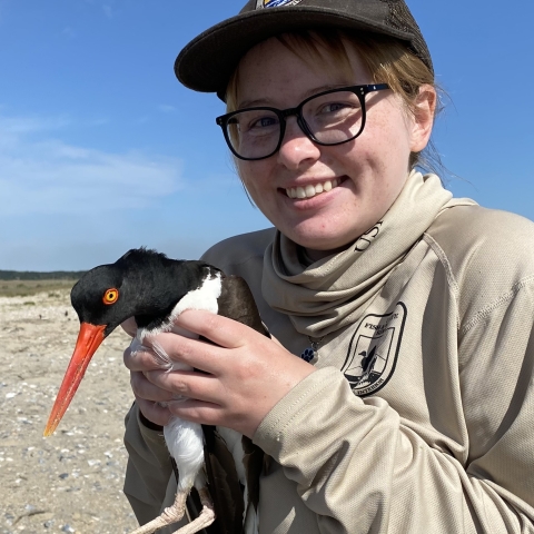 Park Ranger Lydia Hansen smiles and holds an American oystercatcher.