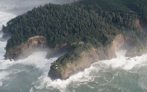 A huge rocky headland covered in trees and surrounded by the rolling Pacific Ocean