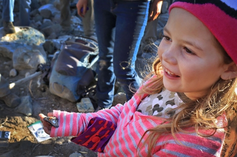 Young girl in pink jacket holds a black, orange and white butterfly in right hand