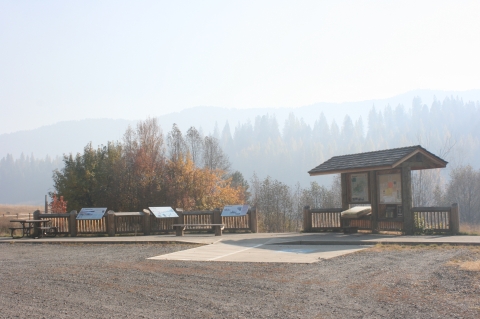 Auto Tour Stop parking area with a shaded kiosk and three interpretive panels in front of a pine forest. 