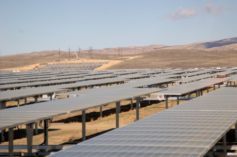 Rows of solar panels in arid grassland with foothills in the distance.